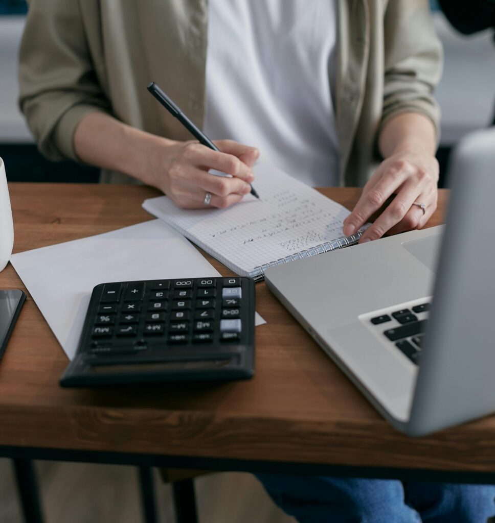 This image shows a person is calculating its budget while sitting with calculator and laptop