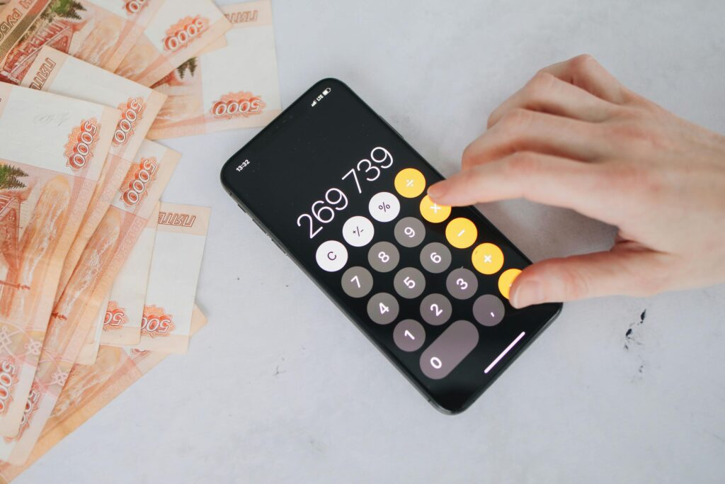This Image shows a person's hand is using the phone calculator and also currency notes in the image